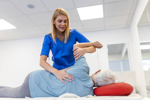 A healthcare professional assists an elderly patient with arm exercises on a treatment table.