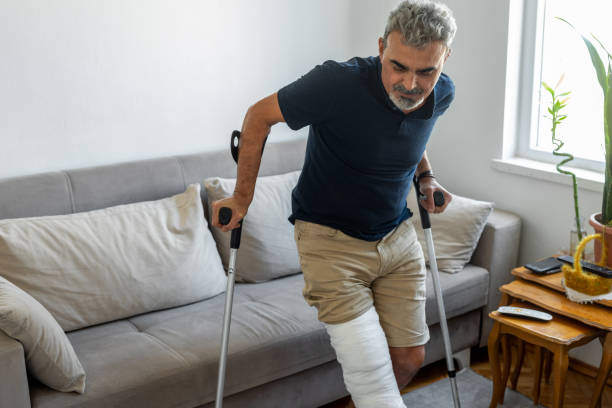 A man with crutches and a bandaged leg navigates a living room.